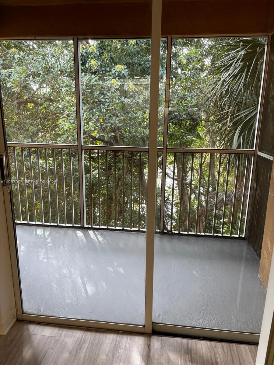 A screened-in balcony with gray flooring overlooks dense green trees and foliage — 3985 W Mcnab Rd # A302, Pompano Beach FL 33069, POMPANO BEACH, FL