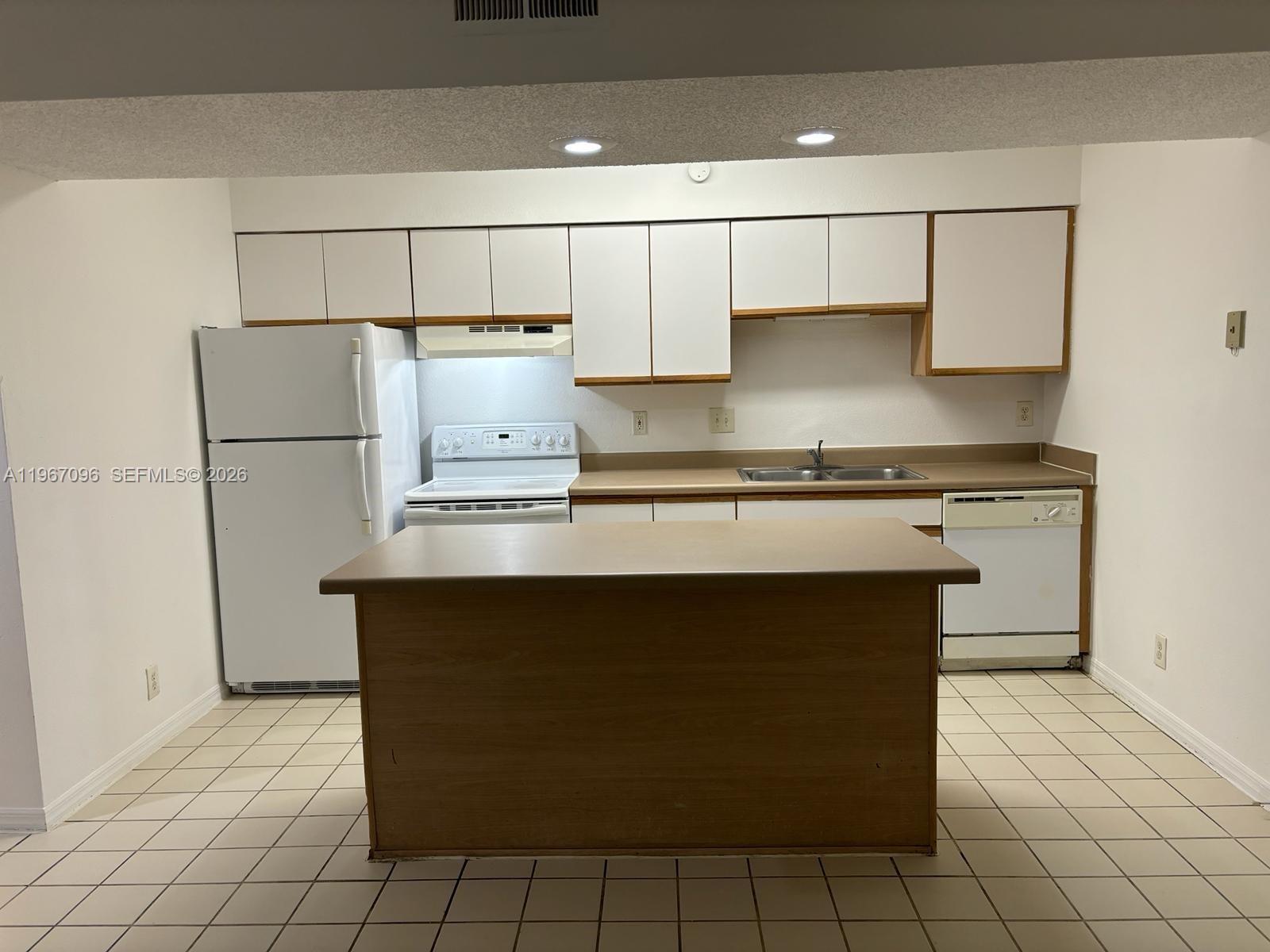 A kitchen features white appliances, wood-toned cabinets, a central island, and light-colored tile flooring — 3985 W Mcnab Rd # A302, Pompano Beach FL 33069, POMPANO BEACH, FL