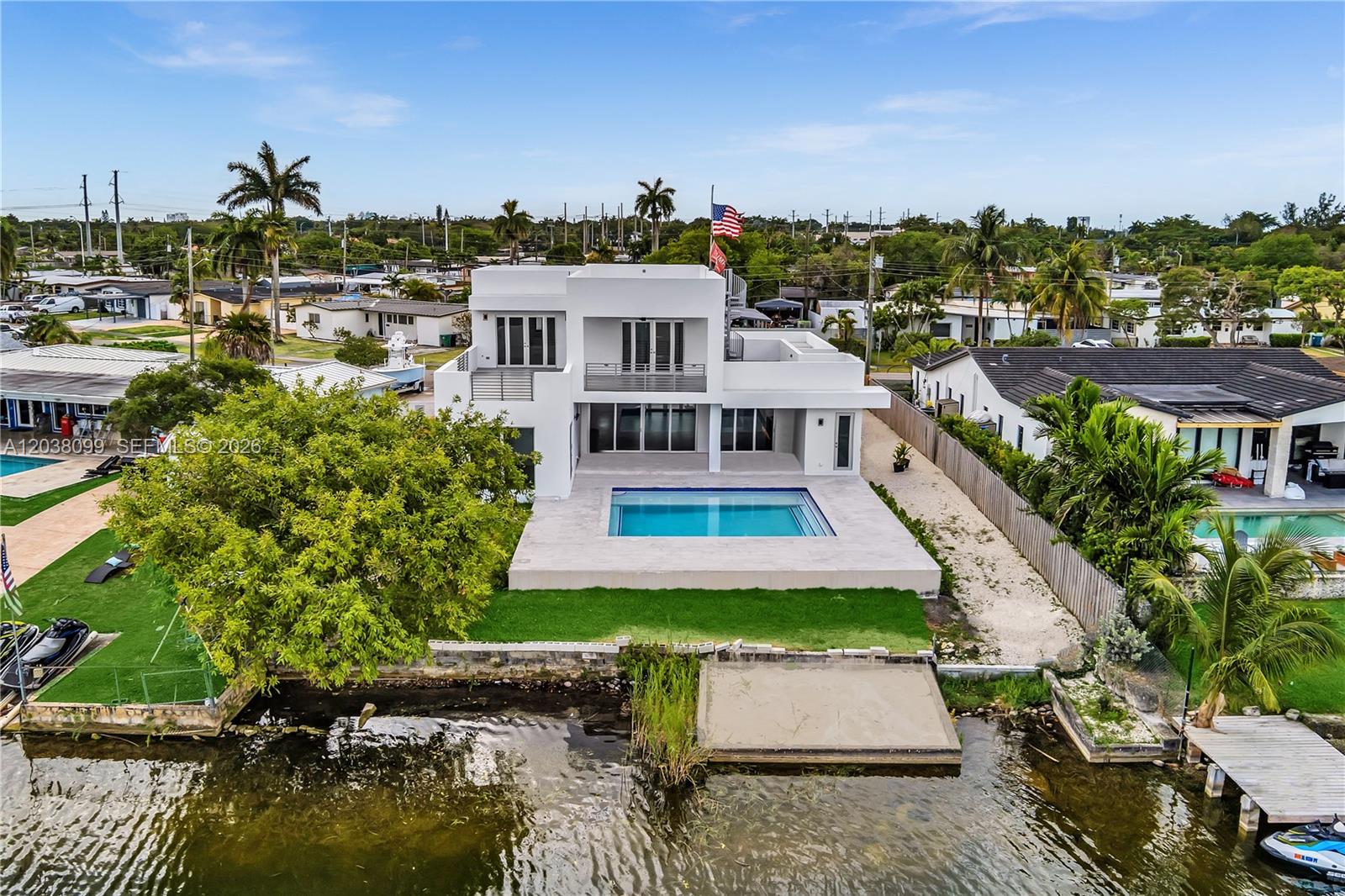 An aerial view of a modern white two-story house with a pool and waterfront dock — 10755 SW 52nd Ter, Miami FL 33165, MIAMI, FL