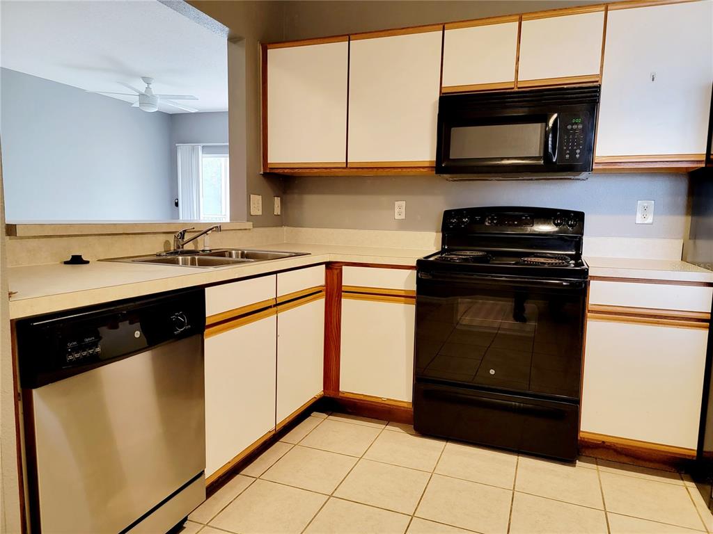 A kitchen features white cabinets with wood trim, black appliances, and a stainless steel dishwasher — 6410 CYPRESSDALE DRIVE UNIT 201, RIVERVIEW, FL