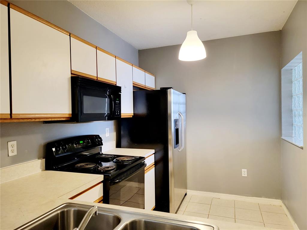A kitchen features white cabinets, black appliances, a stainless steel sink, and a glass-block window — 6410 CYPRESSDALE DRIVE UNIT 201, RIVERVIEW, FL