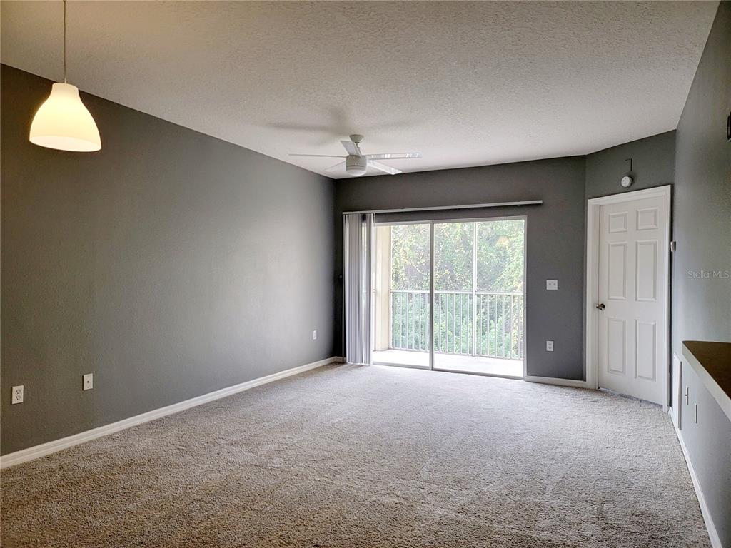 A living room with gray walls, beige carpet, a ceiling fan, and a sliding glass door — 6410 CYPRESSDALE DRIVE UNIT 201, RIVERVIEW, FL