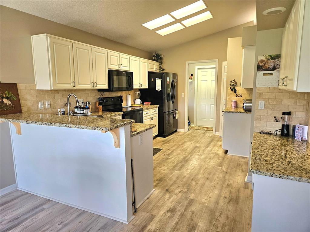A kitchen features white cabinets, granite countertops, a black refrigerator, and light wood-look flooring — 11340 TEE TIME CIRCLE, NEW PORT RICHEY, FL
