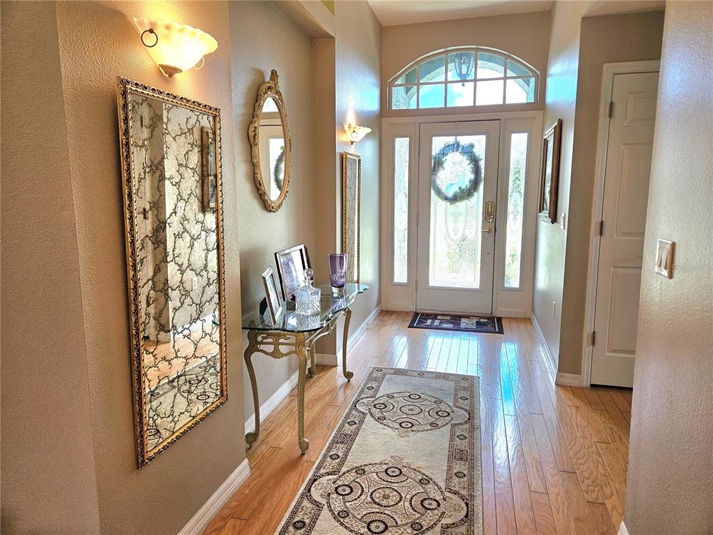 A bright entryway features hardwood floors, a console table, mirrors, and a glass-paneled front door — 11340 TEE TIME CIRCLE, NEW PORT RICHEY, FL