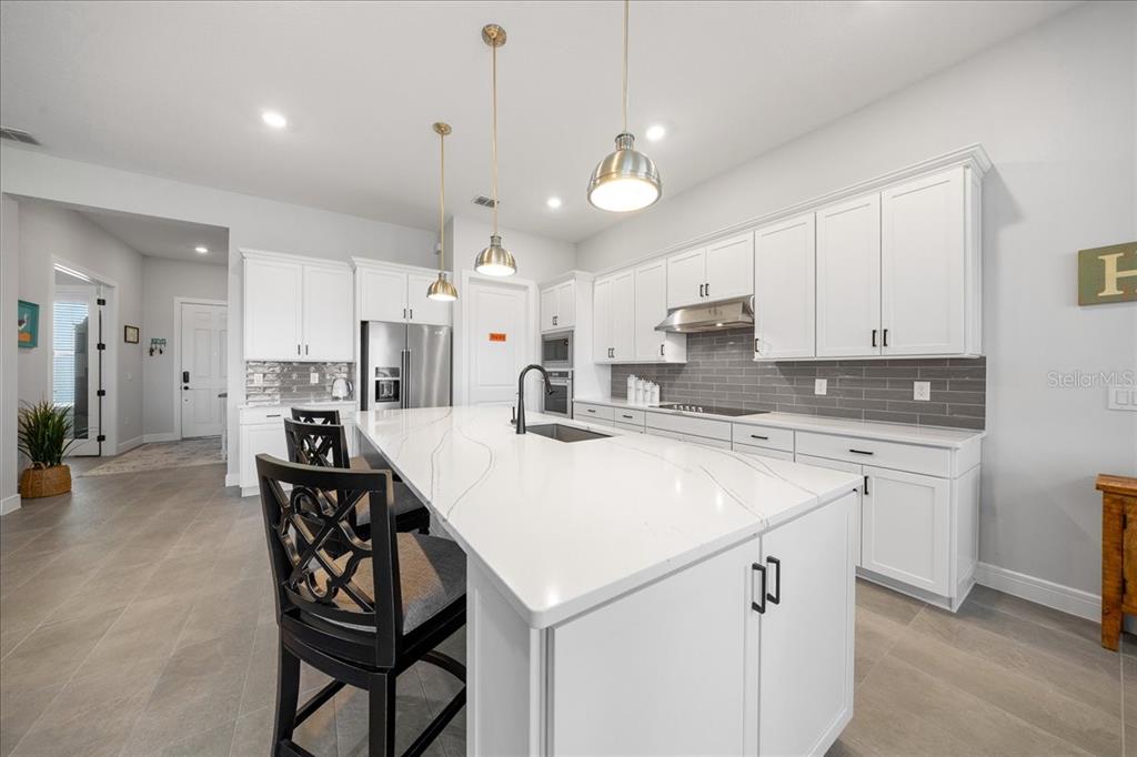 A modern kitchen features white cabinetry, a large quartz island, and gray tile flooring — 6015 SW 86TH CIRCLE, OCALA, FL