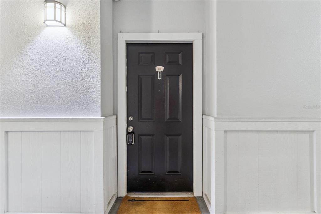 A dark-colored front door with a keypad lock is centered between white paneled walls — 202 E SOUTH STREET UNIT 2039, ORLANDO, FL