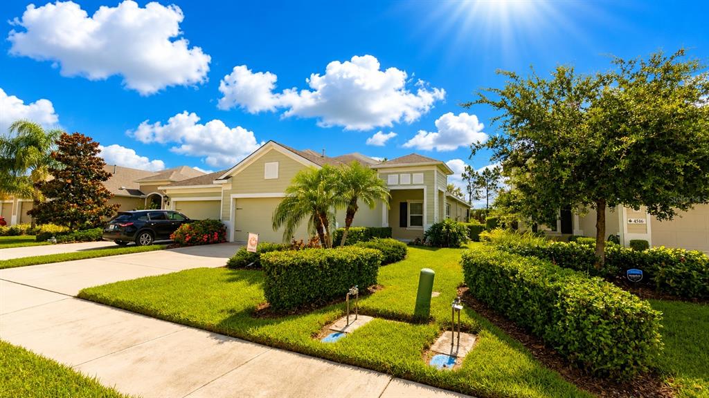 A light green suburban house features a two-car garage, manicured landscaping, and a paved driveway — 4520 DEEP CREEK TERRACE, PARRISH, FL