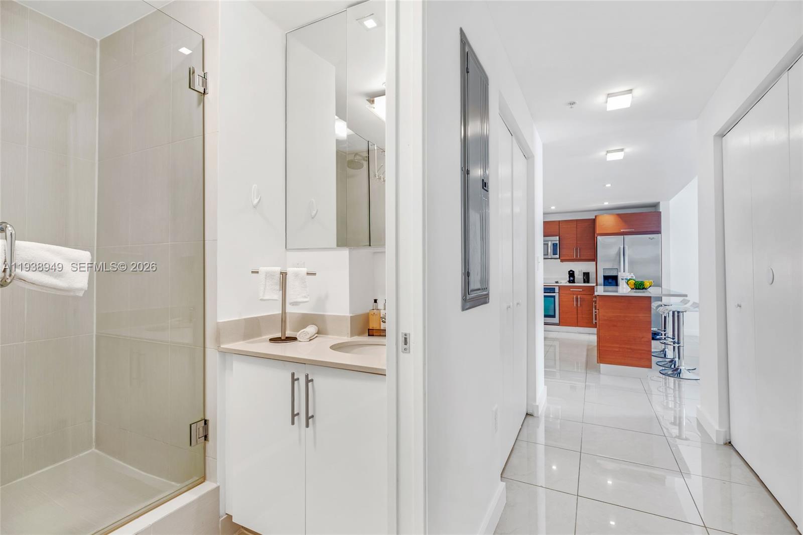 A bathroom with a glass shower stall leads into a kitchen with wood cabinets — 3250 NE 1st Ave # 603, Miami FL 33137, MIAMI, FL