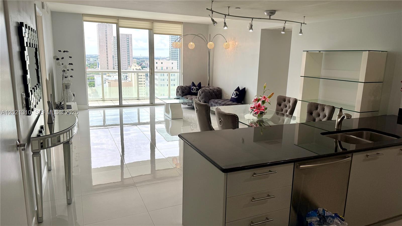A modern living and dining area features white tile floors, a kitchen island, and balcony views — 50 Biscayne Blvd # 2501, Miami FL 33132, MIAMI, FL