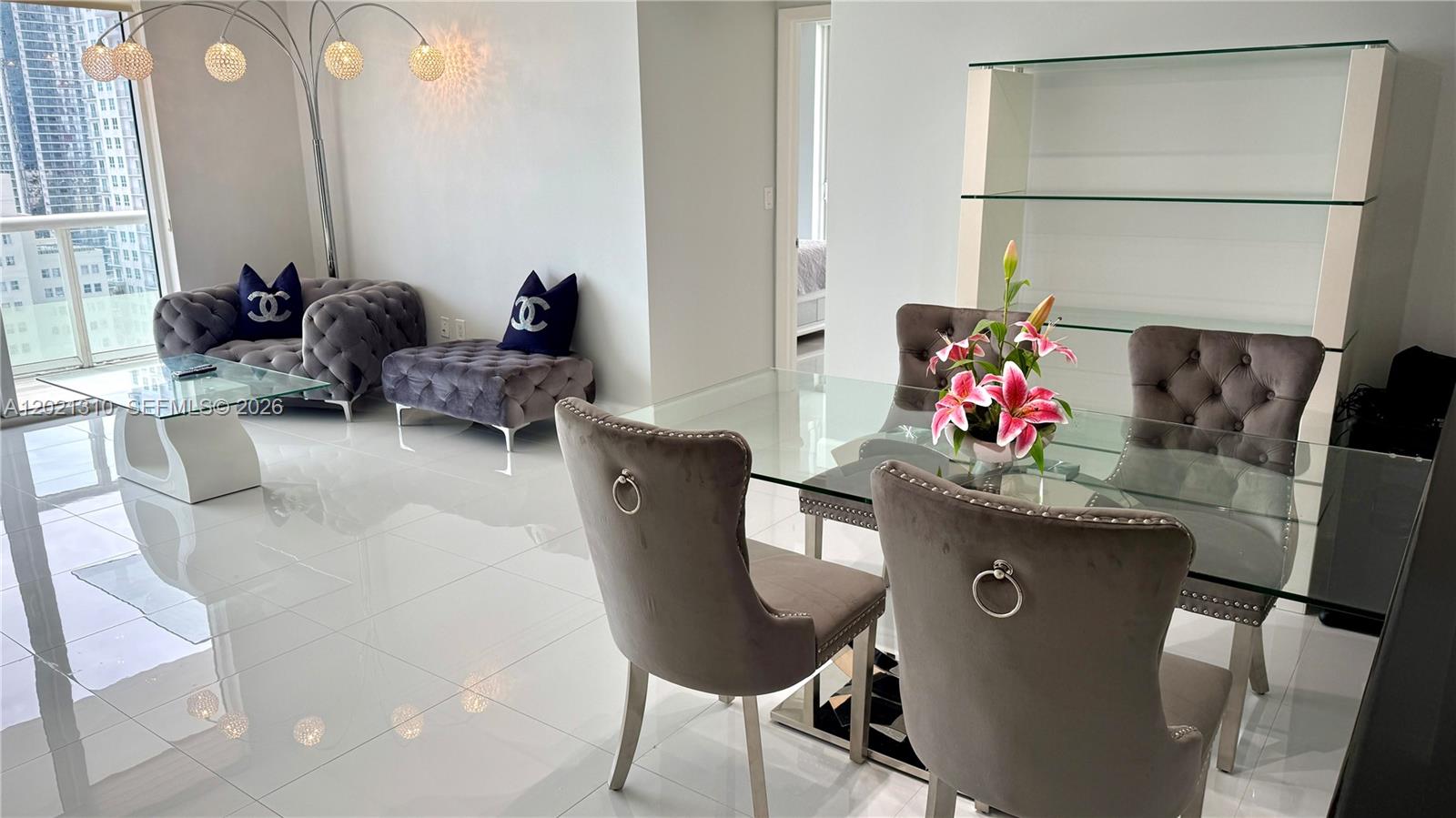 A modern dining and living area features glass tables, grey tufted furniture, and white floors — 50 Biscayne Blvd # 2501, Miami FL 33132, MIAMI, FL
