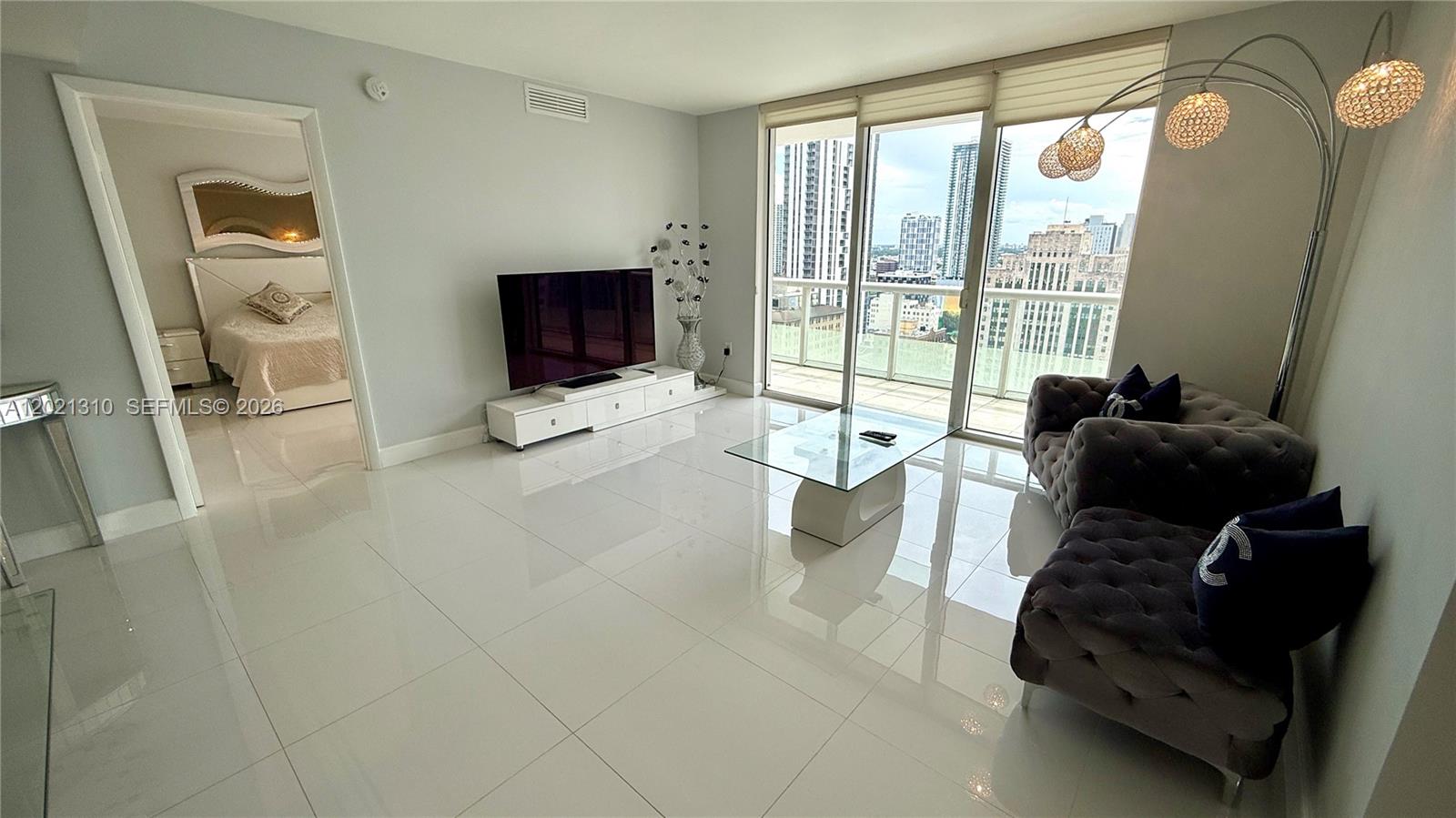 A modern living room features white tile floors, a glass coffee table, and city views — 50 Biscayne Blvd # 2501, Miami FL 33132, MIAMI, FL