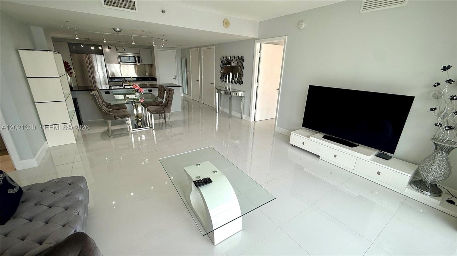 A modern living room features white tile floors, a glass coffee table, and a television — 50 Biscayne Blvd # 2501, Miami FL 33132, MIAMI, FL