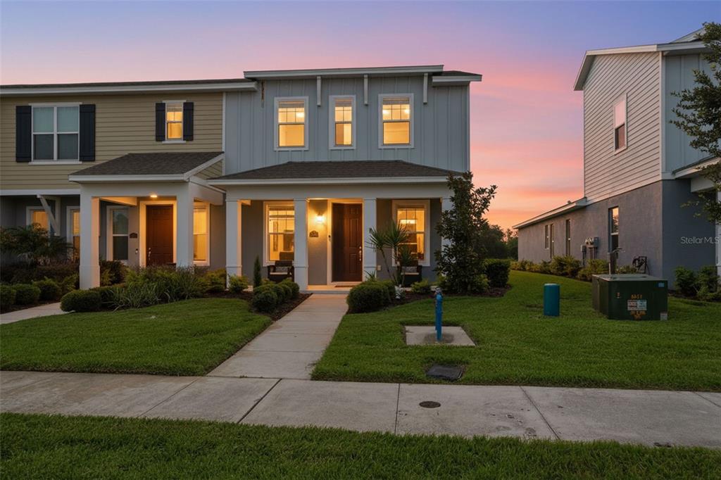 A two-story townhouse with a covered front porch, light-colored siding, and a manicured lawn — 4997 AVALON PARK BOULEVARD, WESLEY CHAPEL, FL