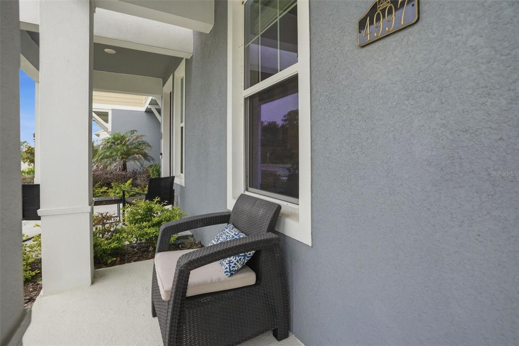 A gray-walled front porch features a dark wicker chair with a patterned cushion — 4997 AVALON PARK BOULEVARD, WESLEY CHAPEL, FL