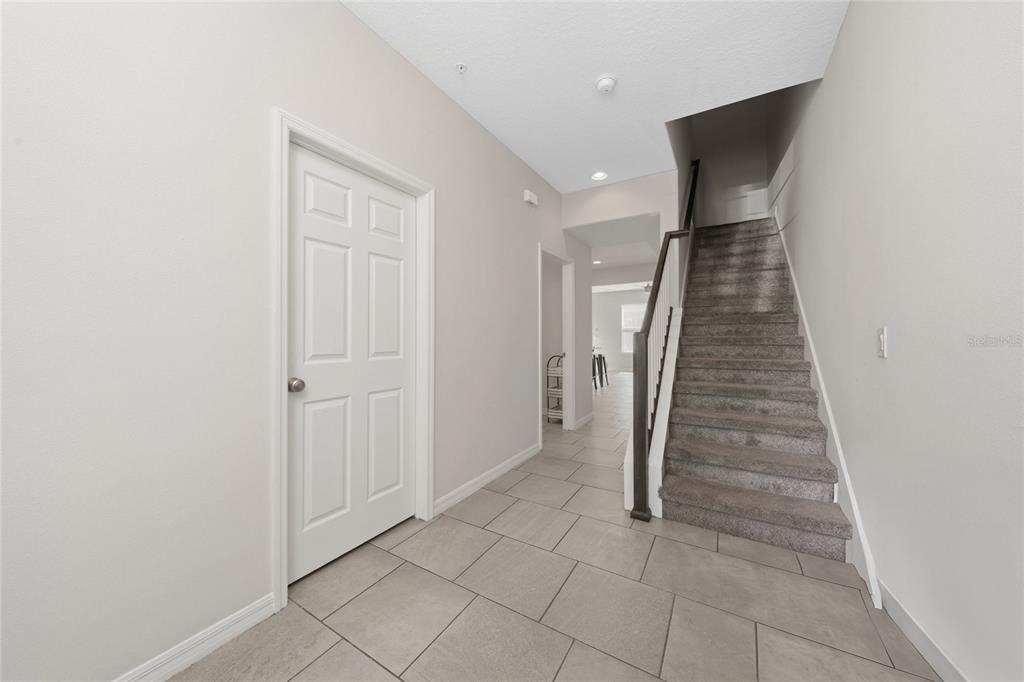 A tiled entryway features a white door, a carpeted staircase, and a hallway leading forward — 8659 VEDDER LANE, ORLANDO, FL