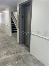 A hallway features a gray elevator door, tiled floors, and a staircase in the background — 227 N MAGNOLIA AVENUE UNIT 206, ORLANDO, FL