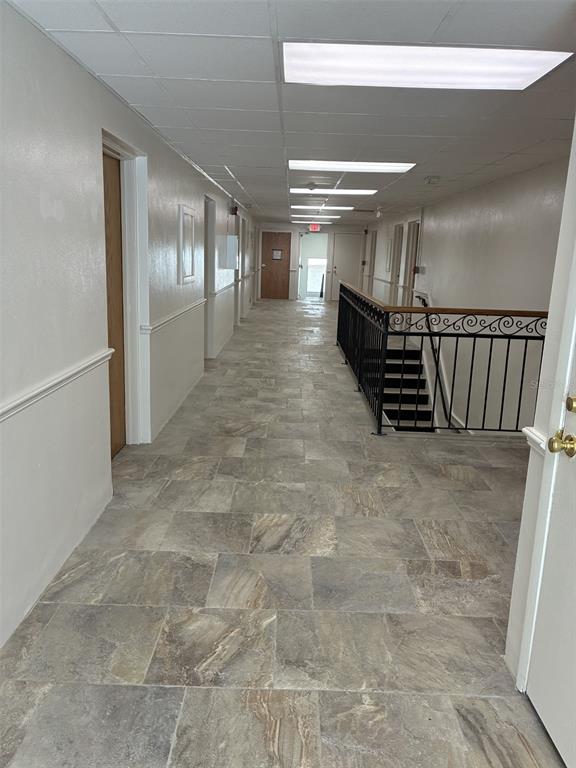A long hallway features light-colored tile flooring, recessed ceiling lights, and a black metal staircase railing — 227 N MAGNOLIA AVENUE UNIT 206, ORLANDO, FL