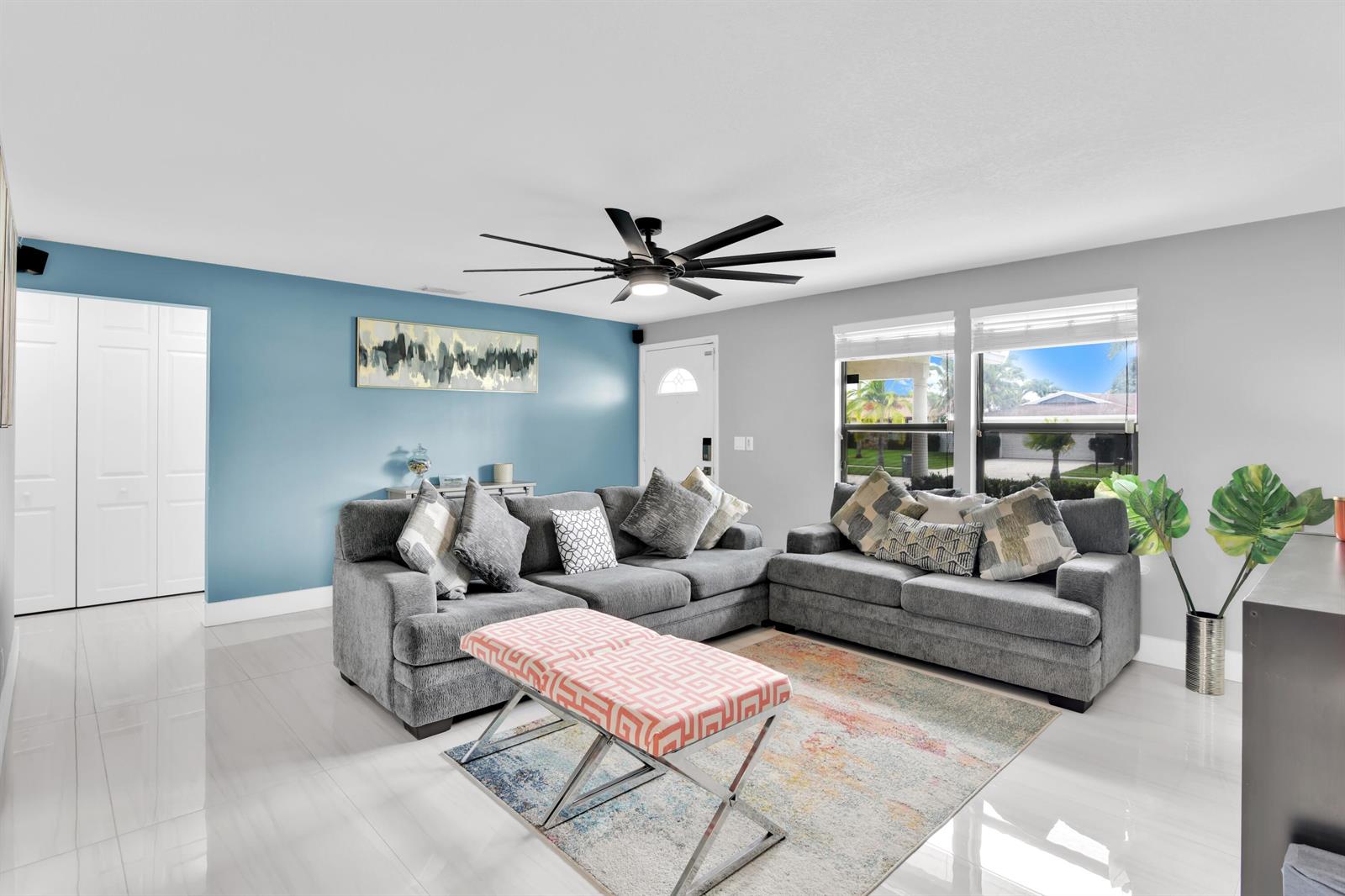 A living room features a blue accent wall, gray sectional sofas, and a patterned ottoman — 8411 Theresa Road, Boynton Beach FL 33472, BOYNTON BEACH, FL