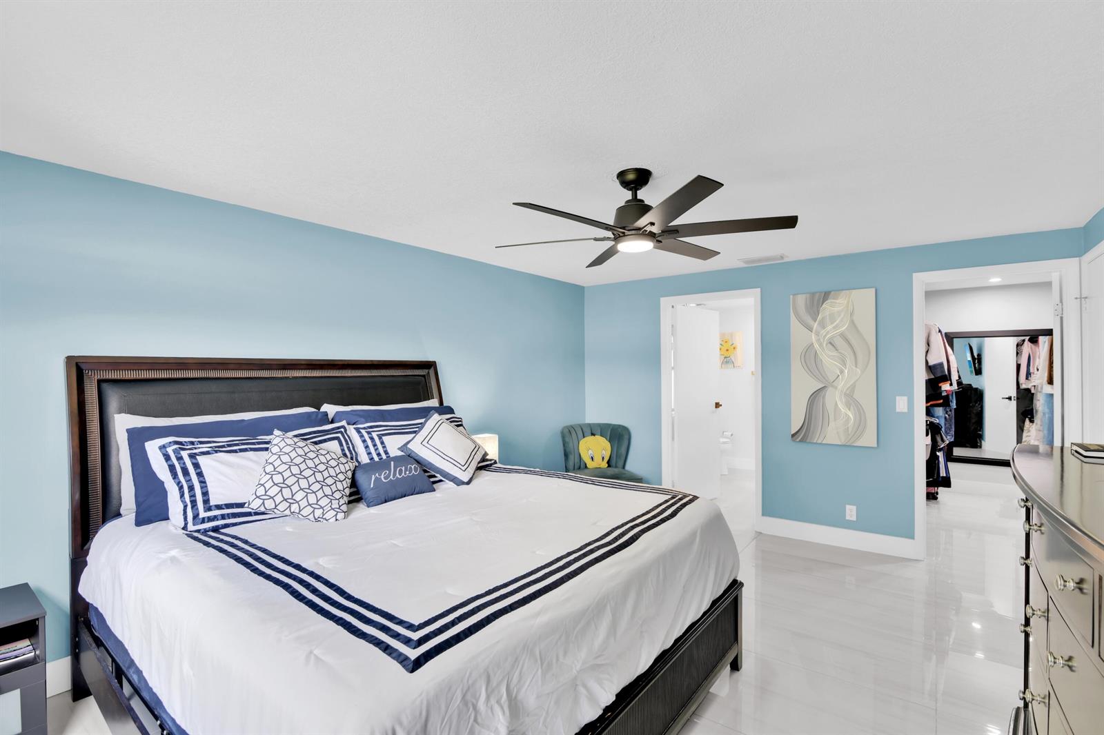 A bedroom with light blue walls, a large bed, a ceiling fan, and tile flooring — 8411 Theresa Road, Boynton Beach FL 33472, BOYNTON BEACH, FL