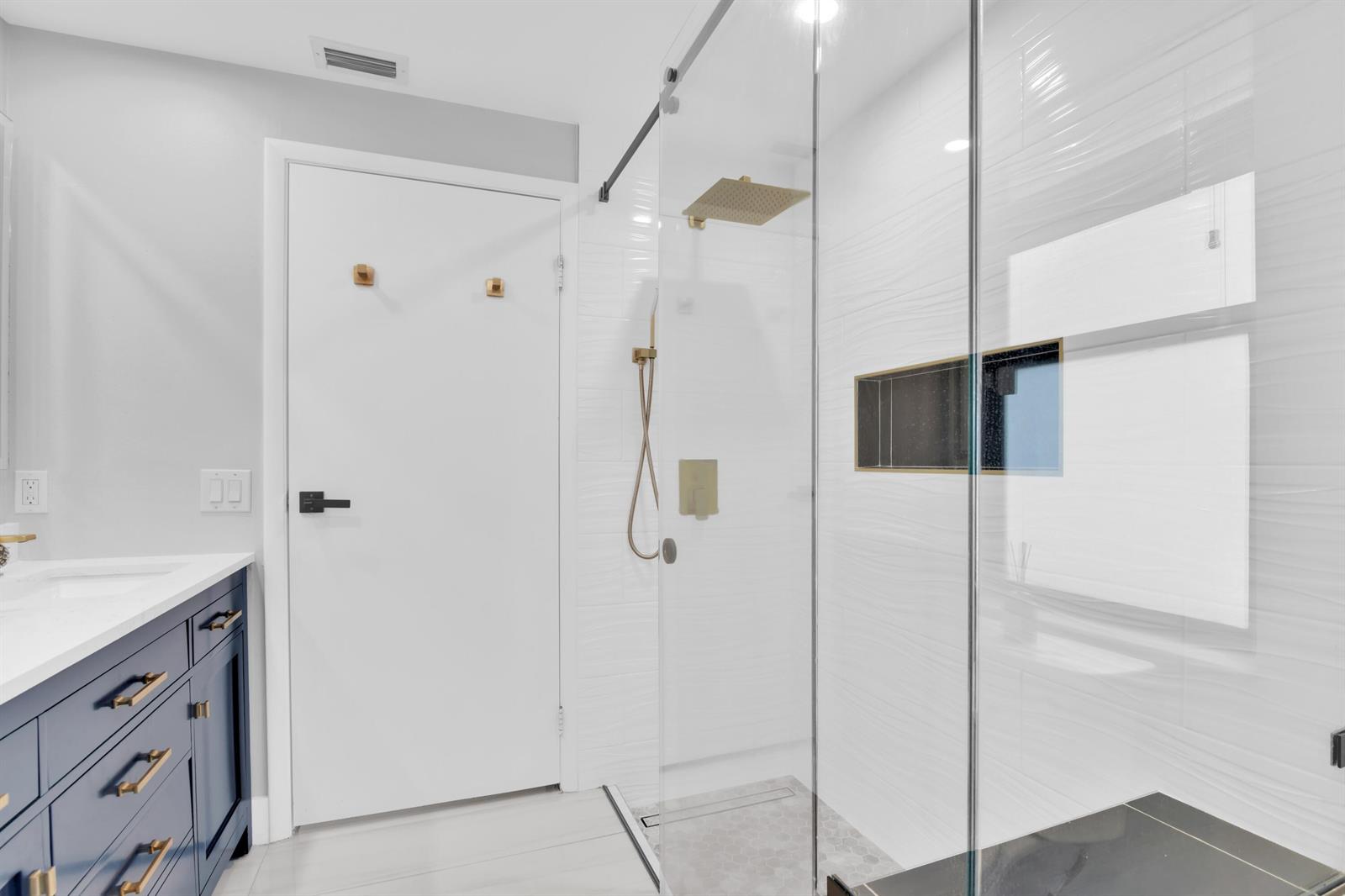 A modern bathroom features a navy blue vanity, a glass-enclosed shower, and gold hardware — 8411 Theresa Road, Boynton Beach FL 33472, BOYNTON BEACH, FL