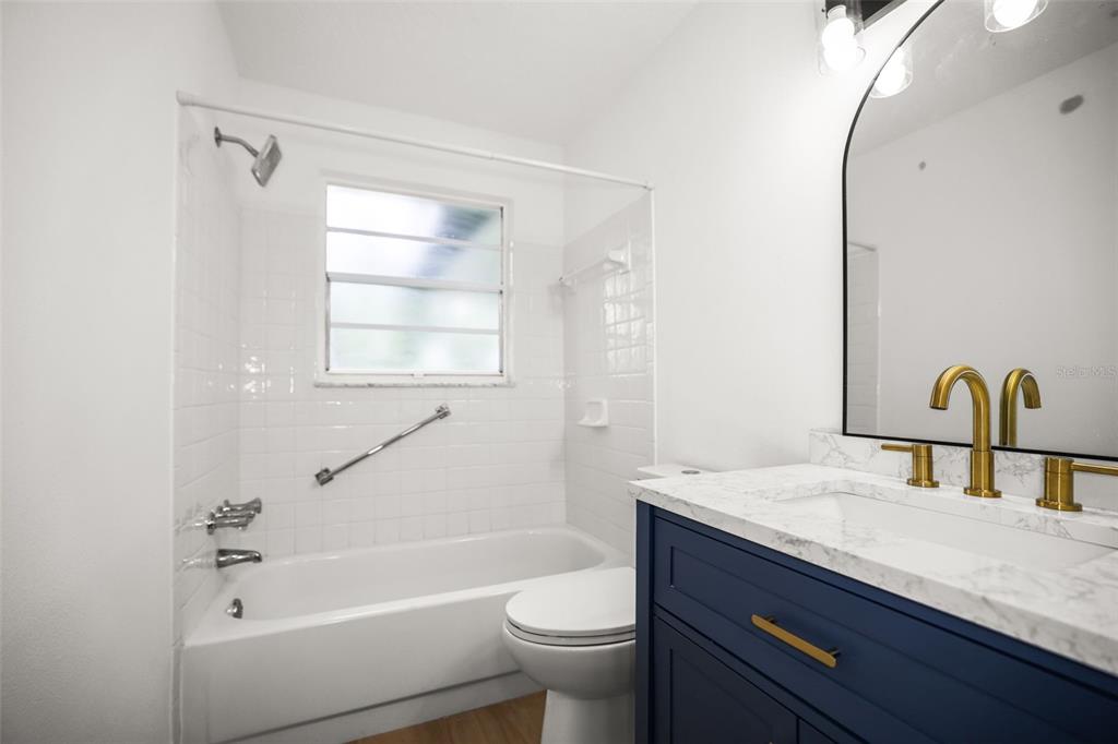 A bathroom features a navy vanity with a marble top, a toilet, and a tub-shower — 3261 LA VERNE COURT, NEW PORT RICHEY, FL