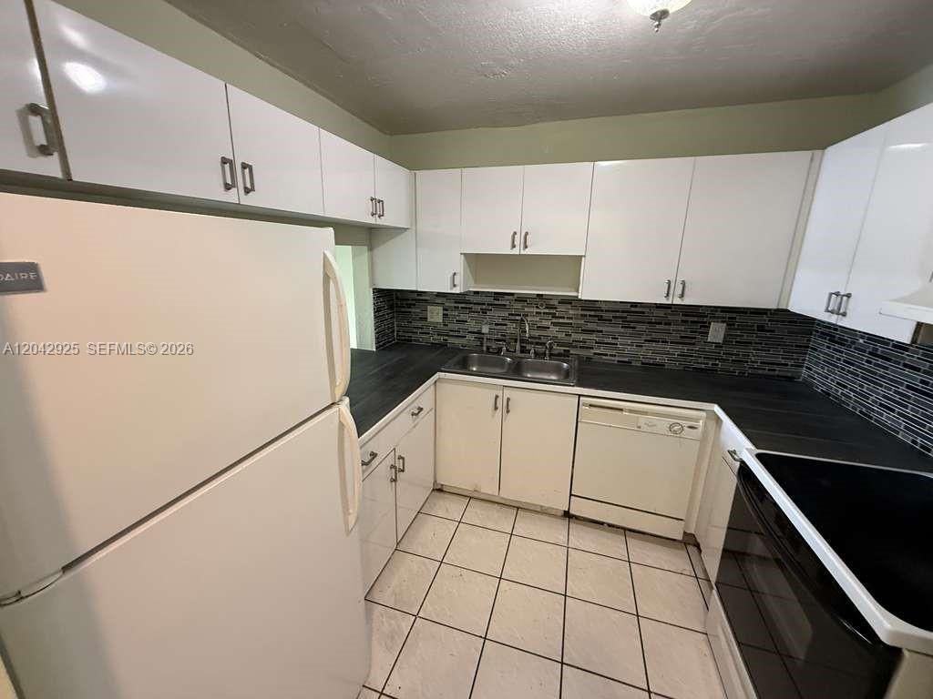 A kitchen features white cabinets, a dark countertop, a tiled backsplash, and white appliances — 1900 W 68th St # G308, Hialeah FL 33014, HIALEAH, FL