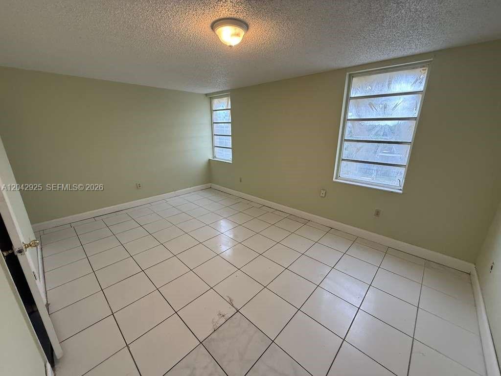 An empty room features white tiled floors, light green walls, and two windows — 1900 W 68th St # G308, Hialeah FL 33014, HIALEAH, FL