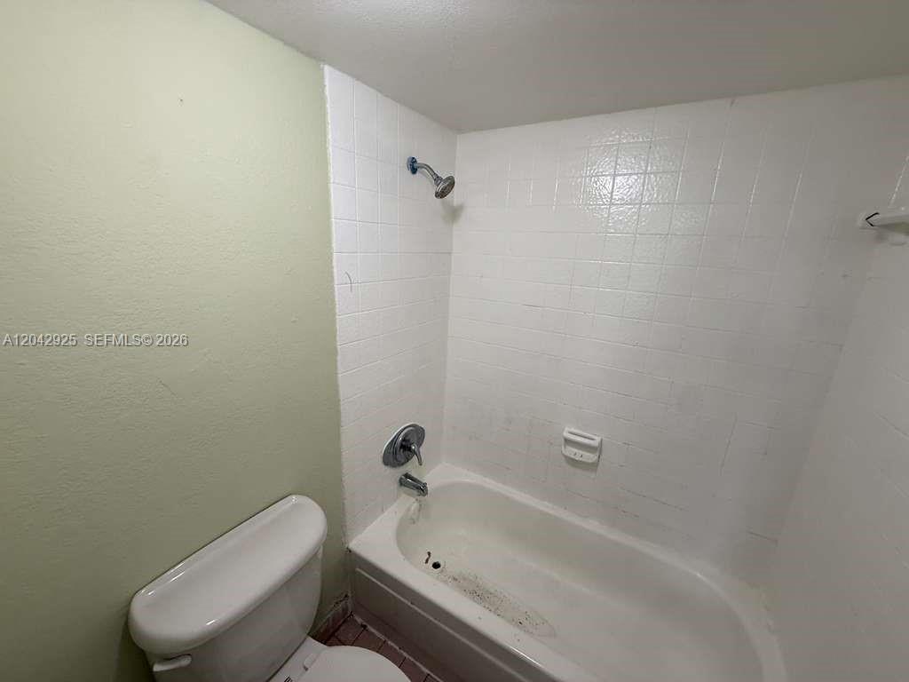 A bathroom features a white bathtub with a showerhead and white tiled walls — 1900 W 68th St # G308, Hialeah FL 33014, HIALEAH, FL