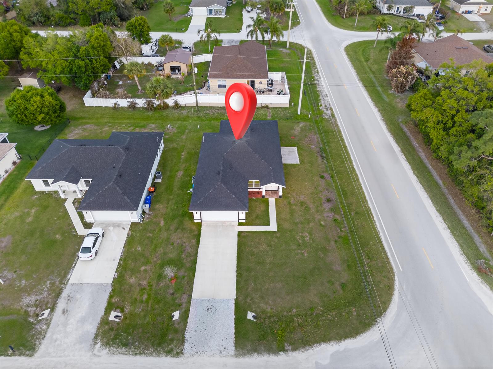 An aerial view shows two suburban houses with dark roofs and driveways near a road — 8316 103rd Avenue, Vero Beach FL 32967, VERO BEACH, FL