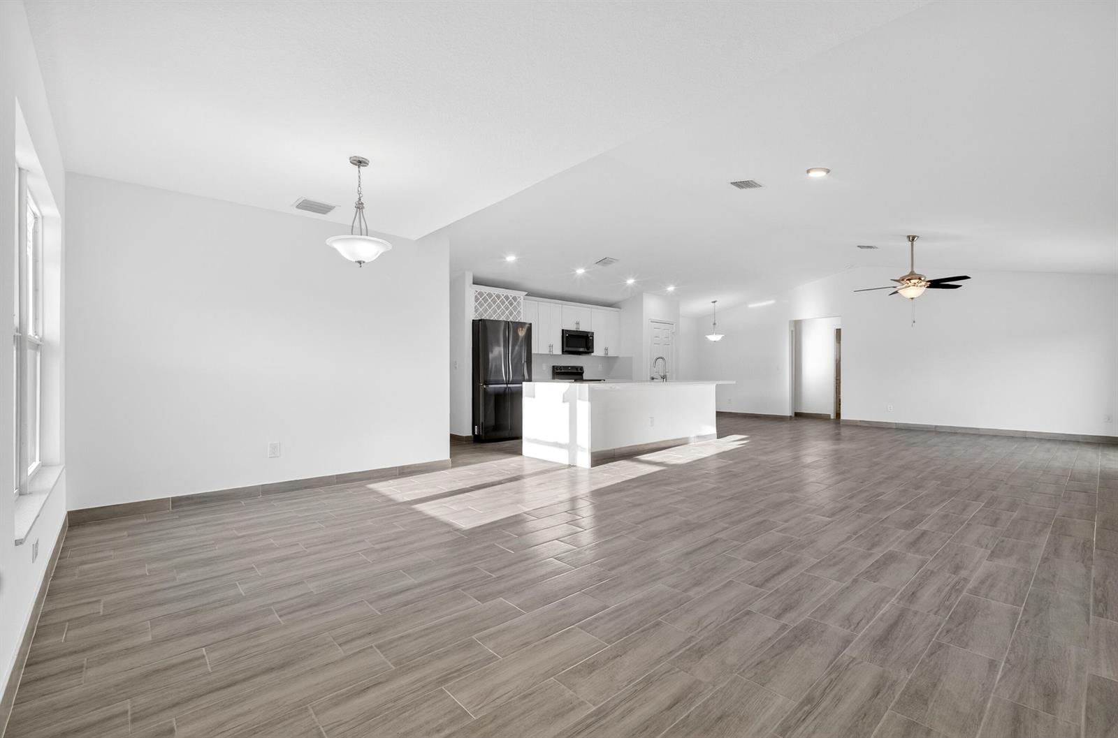 An open-concept kitchen and living area features white cabinetry, a central island, and tile flooring — 8316 103rd Avenue, Vero Beach FL 32967, VERO BEACH, FL