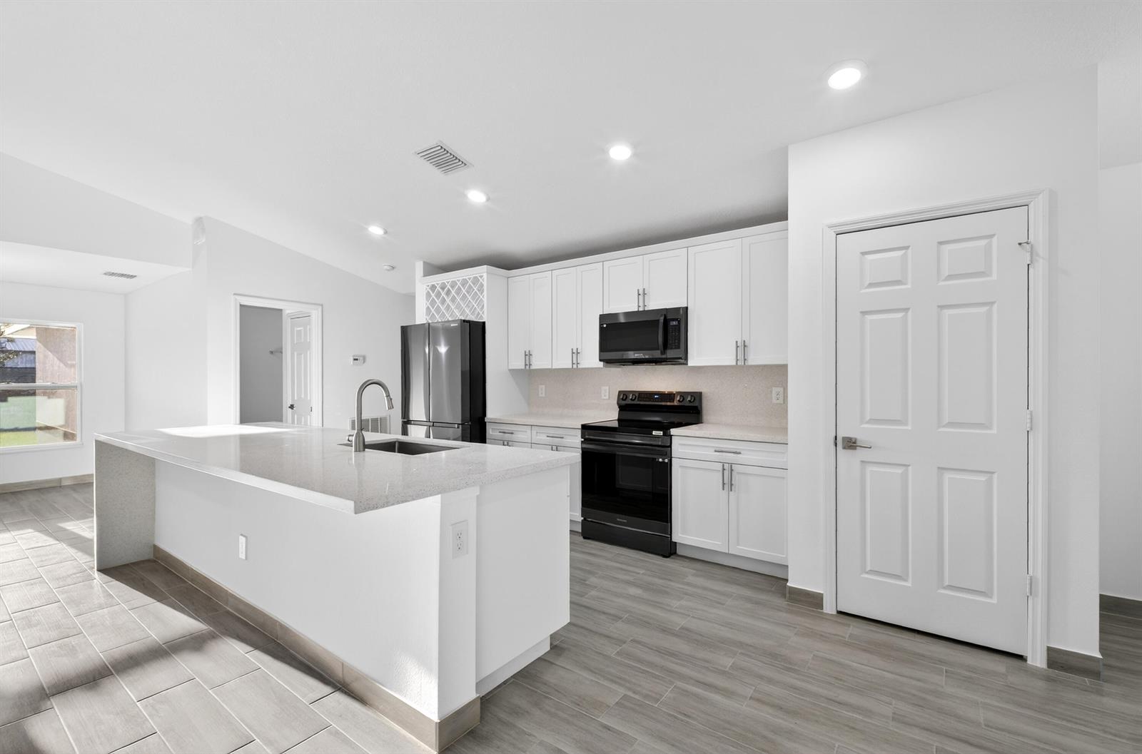 A modern kitchen features white cabinets, black appliances, a quartz island, and gray tile flooring — 8316 103rd Avenue, Vero Beach FL 32967, VERO BEACH, FL