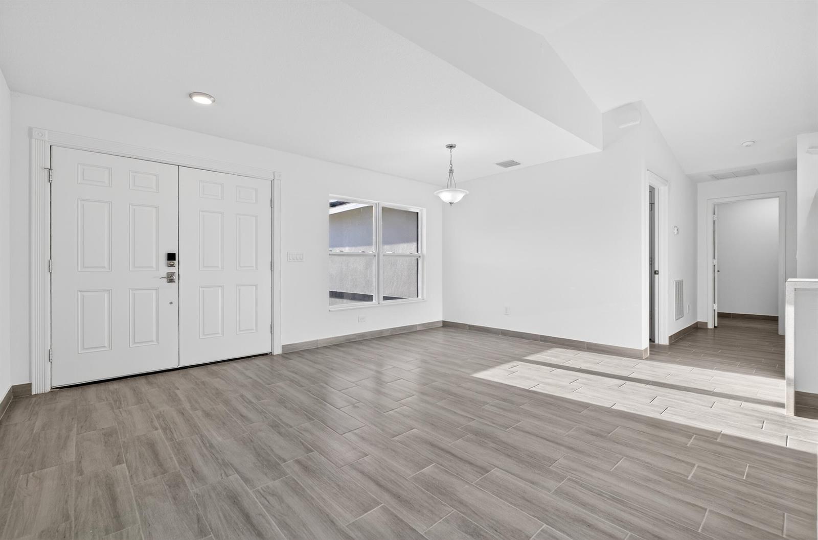 A bright, empty room features white walls, wood-look tile flooring, a double front door, and windows — 8316 103rd Avenue, Vero Beach FL 32967, VERO BEACH, FL