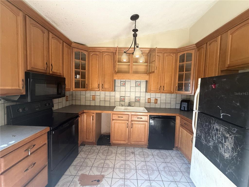 A kitchen features wooden cabinets, black appliances, a white sink, and tiled flooring — 14705 PENGUIN PLACE, TAMPA, FL