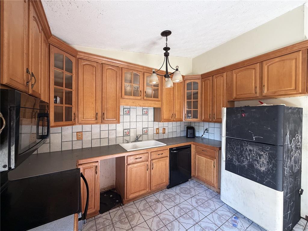 A kitchen features wood cabinets, a white sink, black appliances, and tiled flooring — 14705 PENGUIN PLACE, TAMPA, FL