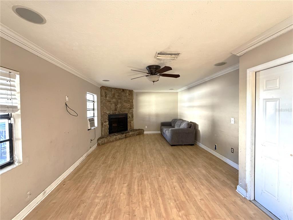 A living room with light wood-look flooring, a corner stone fireplace, and a grey sofa — 14705 PENGUIN PLACE, TAMPA, FL