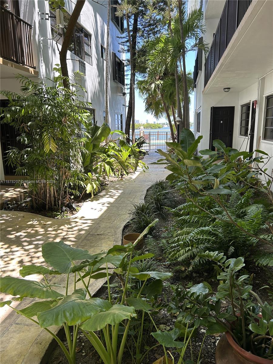 A narrow outdoor walkway between two white buildings leads toward a waterfront view — 7845 NE Bayshore Ct # 20, Miami FL 33138, MIAMI, FL