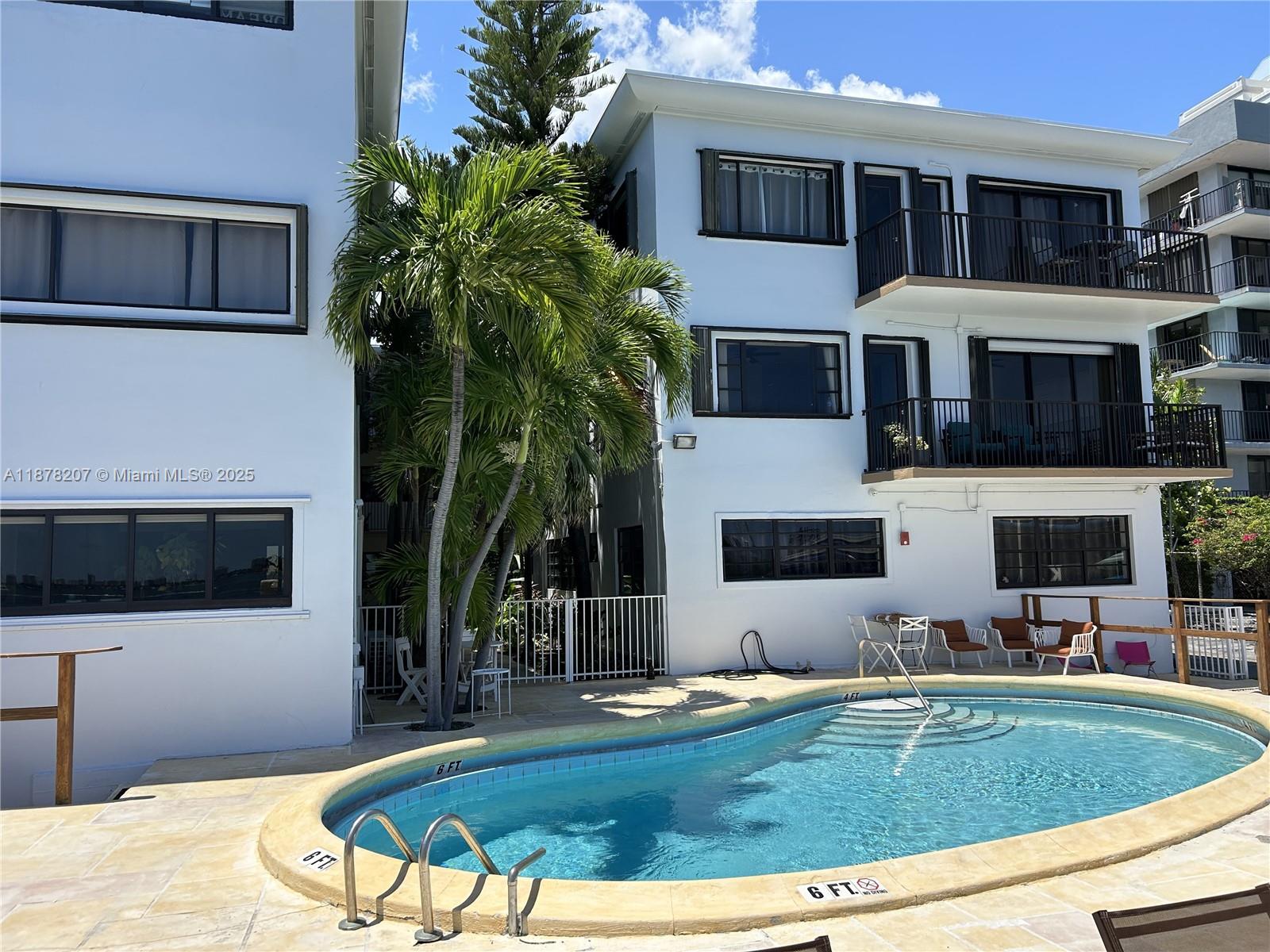 A swimming pool sits in front of a multi-story white apartment building with balconies — 7845 NE Bayshore Ct # 20, Miami FL 33138, MIAMI, FL