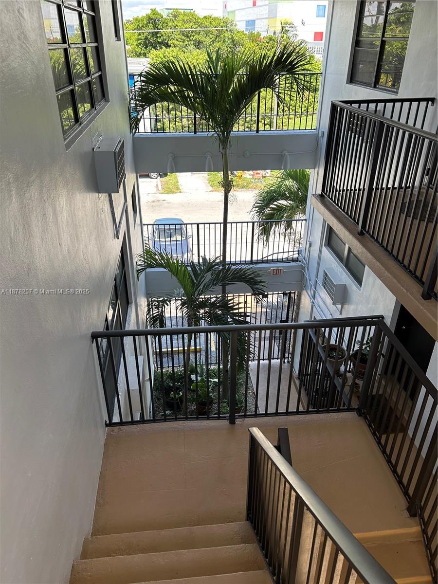 An outdoor stairwell with metal railings overlooks a courtyard featuring palm trees and a gate — 7845 NE Bayshore Ct # 20, Miami FL 33138, MIAMI, FL