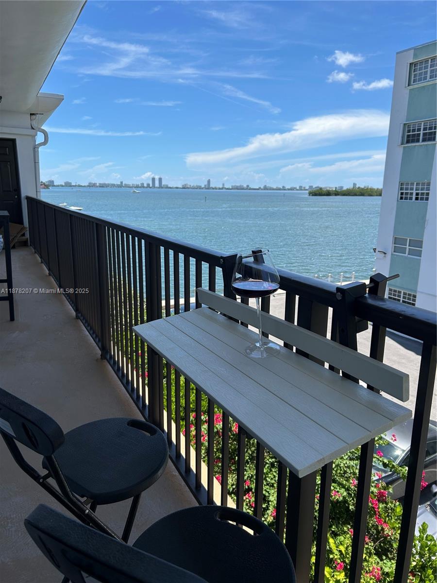 A balcony features a small white table with a wine glass overlooking the water — 7845 NE Bayshore Ct # 20, Miami FL 33138, MIAMI, FL