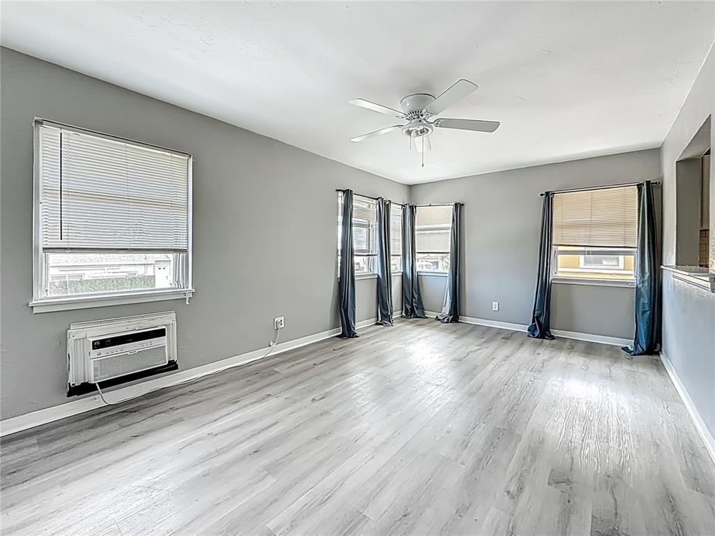 A living room with gray walls, light wood-look flooring, a ceiling fan, and window air conditioner — 107 154TH AVENUE UNIT 2, MADEIRA BEACH, FL