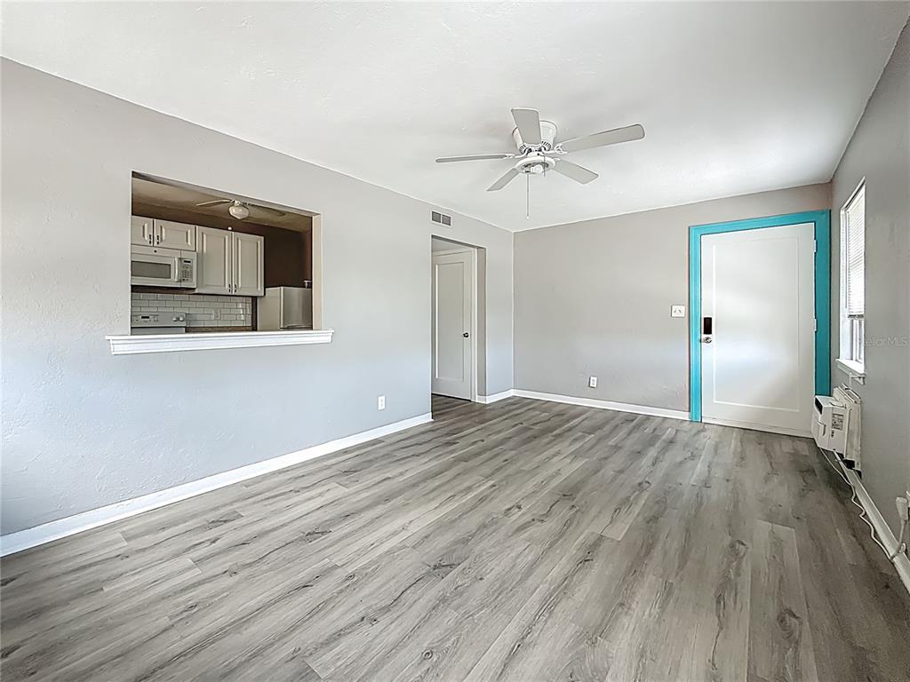 A living room features gray walls, wood-look flooring, a ceiling fan, and a kitchen pass-through — 107 154TH AVENUE UNIT 2, MADEIRA BEACH, FL