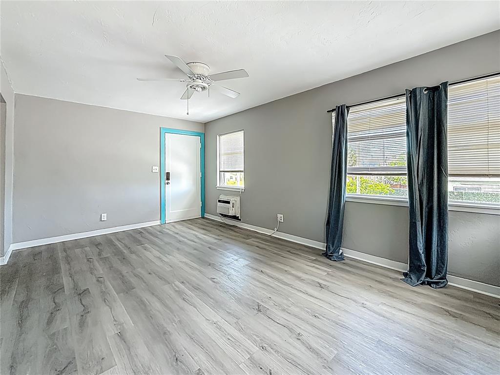 An empty room features gray walls, wood-look flooring, a ceiling fan, and a blue-trimmed door — 107 154TH AVENUE UNIT 2, MADEIRA BEACH, FL