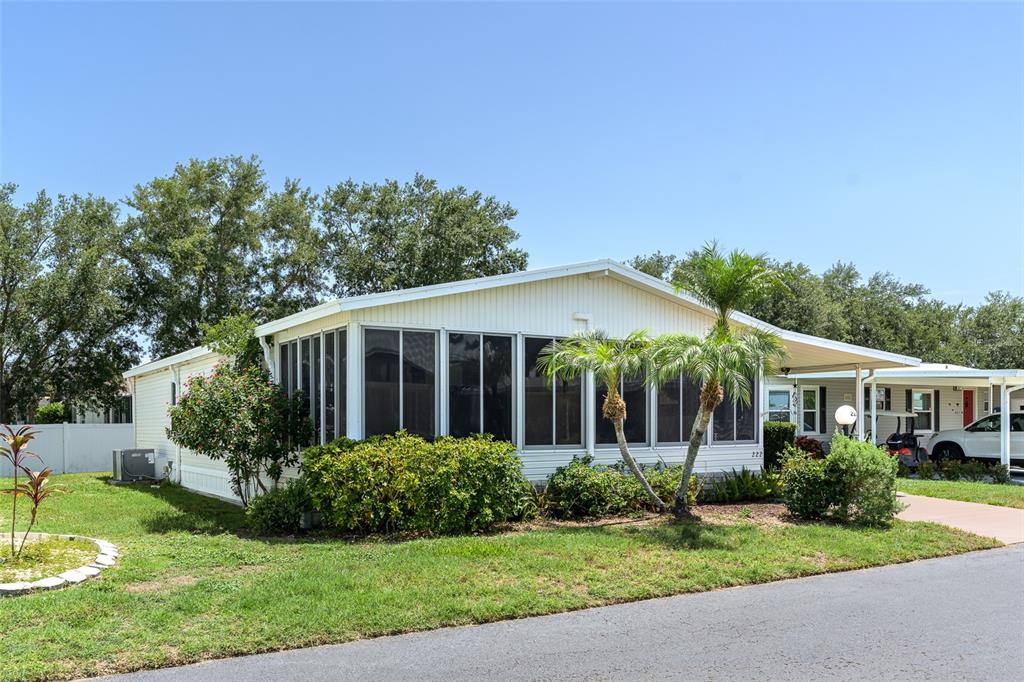 A single-story manufactured home with a screened-in porch and a carport under a clear sky — 5707 45TH STREET E UNIT 222, BRADENTON, FL