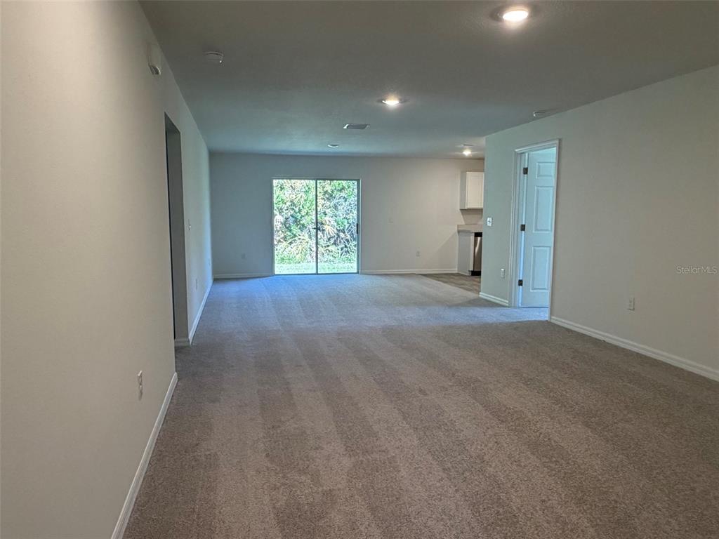 An open-concept living area features neutral carpet, recessed lighting, and a sliding glass door — 880 HUDSON VALLEY DRIVE, POINCIANA, FL