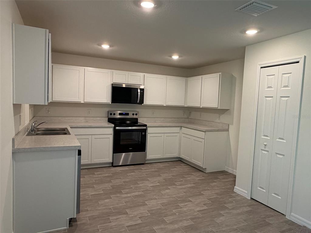 A kitchen with white cabinets, stainless steel appliances, light countertops, and wood-look flooring — 880 HUDSON VALLEY DRIVE, POINCIANA, FL