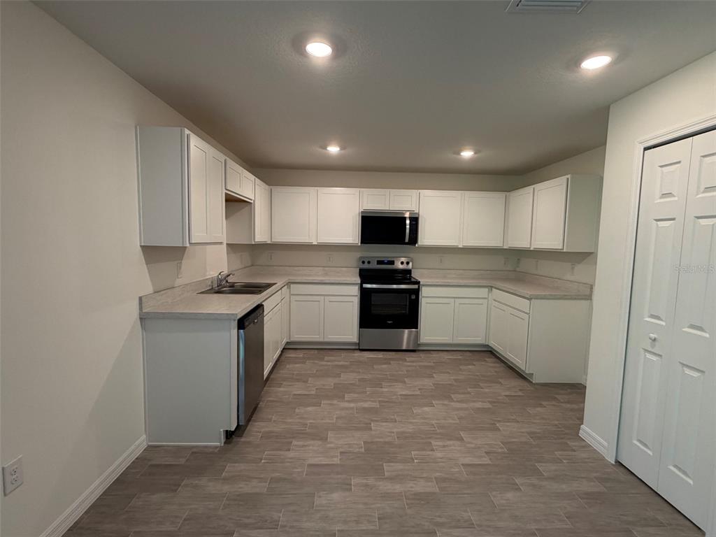 A kitchen features white cabinets, stainless steel appliances, grey countertops, and wood-look tile flooring — 880 HUDSON VALLEY DRIVE, POINCIANA, FL