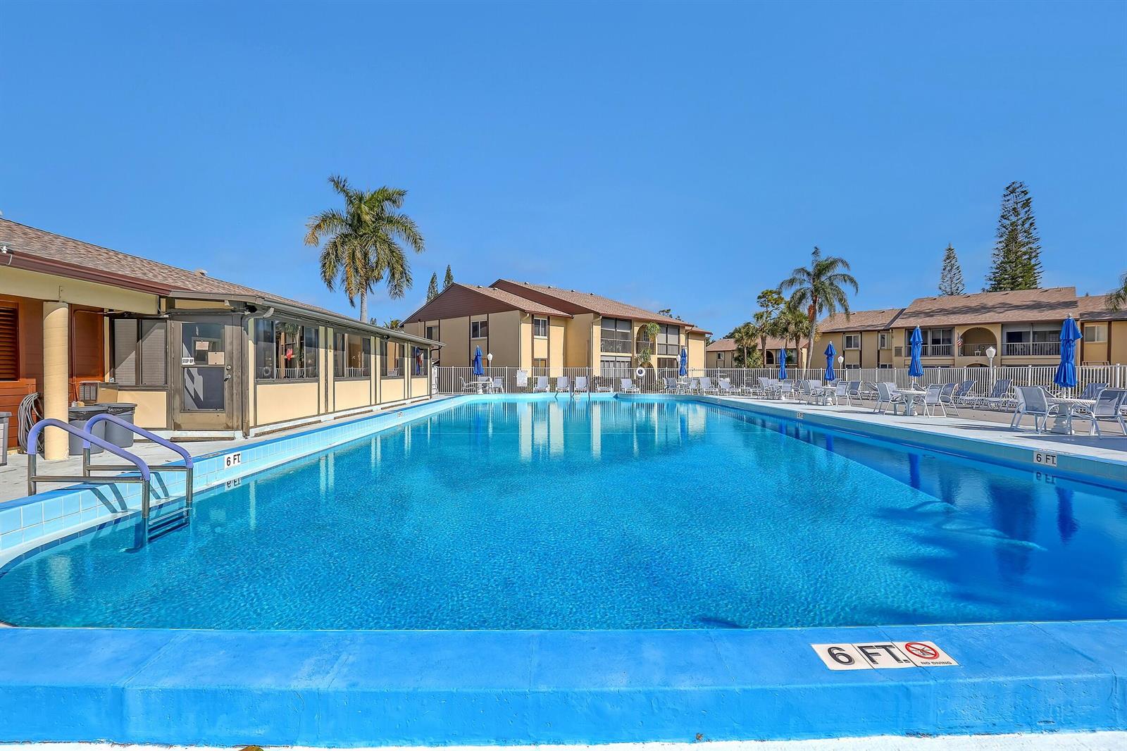 A large rectangular swimming pool sits in front of multi-story apartment buildings under a clear sky — 337 Pine Ridge Circle # 1, FL 33463, FL