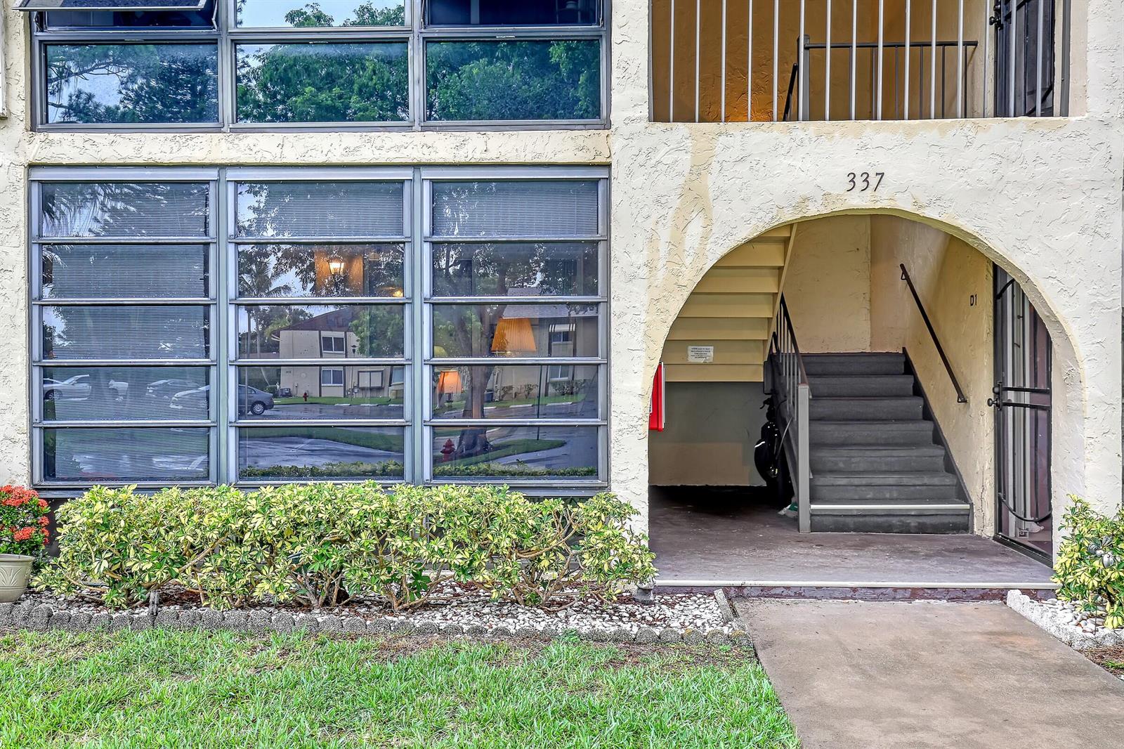 The exterior of a multi-story apartment building features large windows, a landscaped hedge, and stairs — 337 Pine Ridge Circle # 1, FL 33463, FL