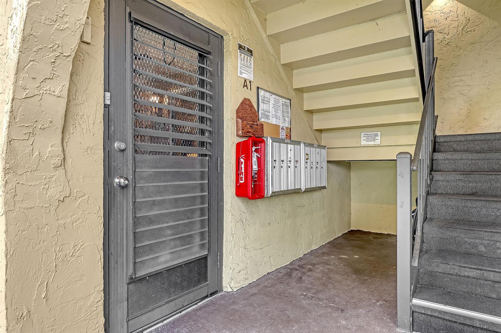An apartment building entrance features a security door, mailboxes, a fire extinguisher, and a staircase — 337 Pine Ridge Circle # 1, FL 33463, FL