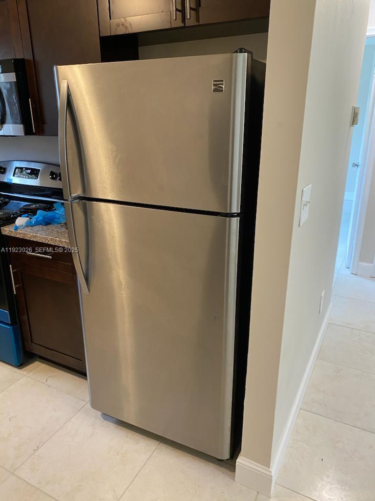 A stainless steel top-freezer refrigerator stands in a kitchen with dark wood cabinets — 2416 NW 79th Ter, Miami FL 33147, MIAMI, FL